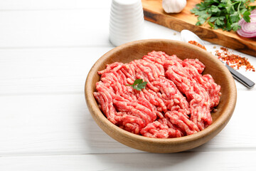 Raw minced meat, parsley and spices on white wooden table, closeup. Space for text