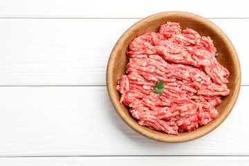 Fresh raw minced meat in bowl on white wooden table, top view. Space for text