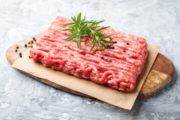 Raw minced meat with peppercorns and rosemary on grey textured table, closeup