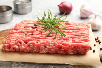 Raw minced meat with rosemary and spices on grey textured table, closeup