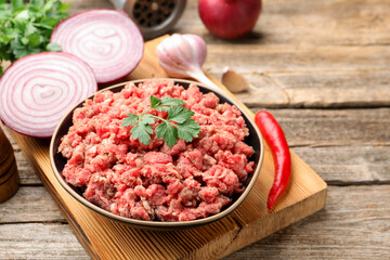 Raw minced meat with parsley in bowl and products on wooden table, closeup. Space for text