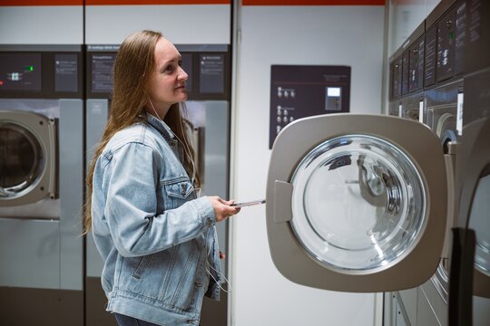 Woman using washing machine in self service laundry with smartphone in hand