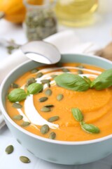 Delicious pumpkin soup with seeds and basil in bowl on table, closeup