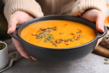 Woman with delicious pumpkin soup at grey table, closeup