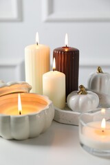 Many different burning candles on white table, closeup. Autumn atmosphere