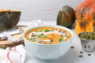 Delicious pumpkin soup with spices, cheese and sour cream in bowl on light table, closeup