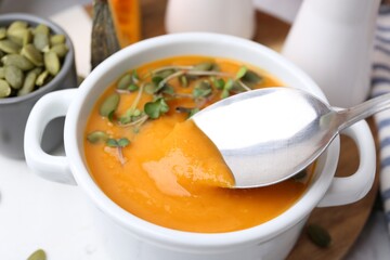 Taking delicious pumpkin soup with spoon from bowl on table, closeup