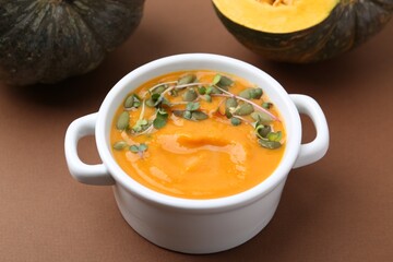 Delicious pumpkin soup with seeds and microgreens in bowl on brown table, closeup