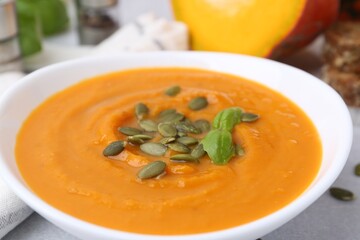 Delicious pumpkin soup with seeds and basil in bowl on table, closeup