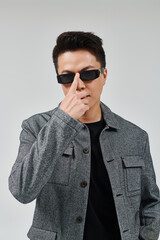 Confident young Asian man showing style while wearing sunglasses against a simple background