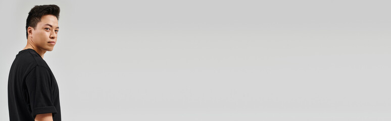 Fototapeta premium Handsome young Asian man standing confidently against a minimalist gray backdrop