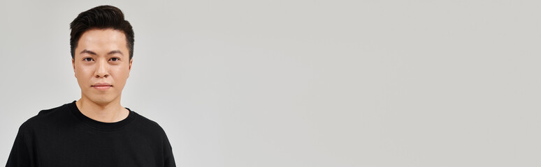 Obraz premium Young Asian man poses confidently in casual attire against a minimalist backdrop