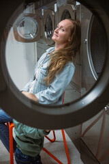 Woman in denim jacket resting on chair in self service laundry
