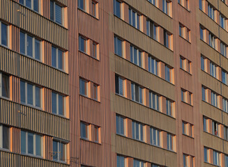 Close-up of colorful apartment building facade with repeating windows and striped panels, creating geometric urban pattern in warm light