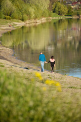A loving couple walks along the riverbank holding hands. Outdoor walks at sunset. Romance and love relationships. Man and woman.