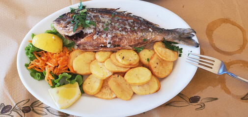 Fried dorado with vegetables and deep-fried potato wedges. Dorado with baked broccoli and carrots. Garnished with lemon and herbs.
