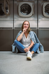 Woman sitting on floor in self service laundromat while waiting laundry