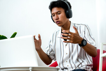 Young Asian Man Wearing Headphones Engaged In Video Call Using Laptop