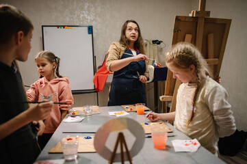 Artist explains how to mix and combine colors. Teacher learn children to draw pictures in an art lesson. Childs painting in workshop. Kids drawing brush on easel. Education, learning concept.