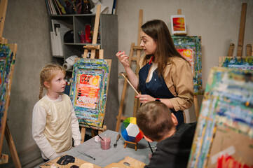 Childs painting in workshop. Artist explains how to mix and combine colors. Kids drawing brush on easel. Education, learning concept.  Teacher learn children to draw pictures in an art lesson.