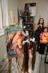A child removes a picture from an easel. Closeup. A girl painted a picture in a workshop in art class. Art lesson. Education and learning concept.