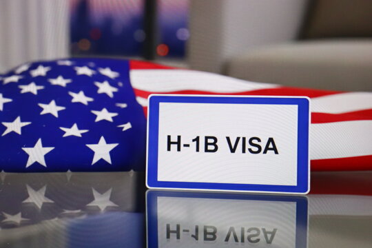H-1B Visa card is on a table, USA flag in background