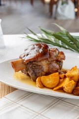 Roasted pork shank with potatoes and gravy on a white plate