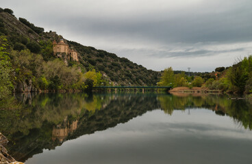 Fototapeta premium The Hermitage of San Saturio is located in a natural setting on the banks of the River Duero, with its reflection in the river, built on a cave on the side of a hill. Soria, Spain. 