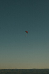 Minimalist view of a paraglider flying high in the evening sky with mountains in the background. Adventure, freedom, and extreme sport concept.
