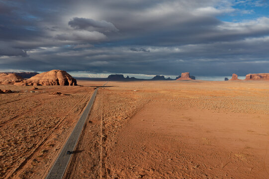 Aerial view of a long road cuts through the arid landscape towards iconic rock formations under a dramatic sky, Sedona, Arizona, United States.