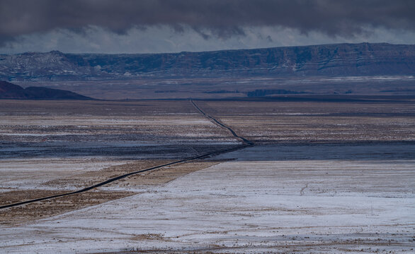 Aerial view of a long road cuts through the snow-dusted desert landscape, leading towards distant mesas under a brooding sky, Sedona, Arizona, United States.