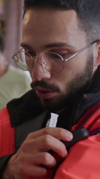 Vertical shot of young multiethnic male paramedic in uniform radioing and using medical equipment while providing first aid to senior patient indoors