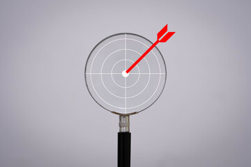 Magnifying glass with a red dart hitting the center of a target, symbolizing focus, accuracy, goal achievement, and strategic analysis.