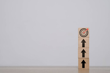 Wooden blocks stacked with upward arrows leading to a bullseye target, symbolizing business success, growth strategy, achieving goals, and performance improvement.