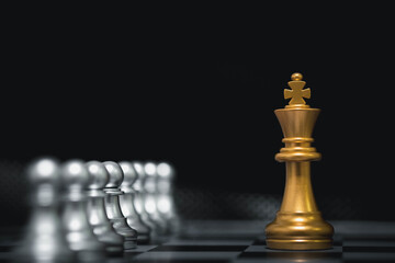 Golden chess king piece standing against silver pawns on a chessboard, symbolizing leadership, strategy, decision making, business success, power, dominance, and competitive advantage.