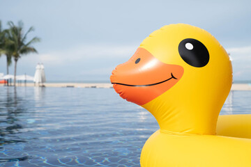 Bright yellow inflatable duck float in a swimming pool with beach background, perfect for summer vacation, travel blogs, pool party promotions, and fun holiday concepts.