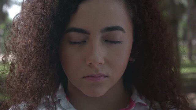 Close-up beauty portrait of a young woman with curly brown hair giving a slight smirk to the camera.