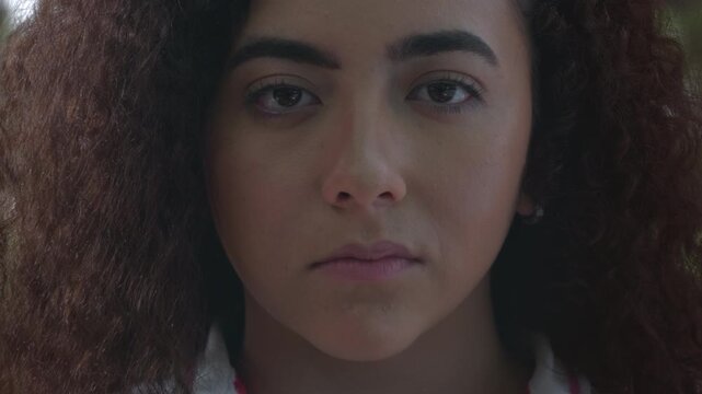 Close-up beauty portrait of a young woman with curly brown hair giving a slight smirk to the camera.