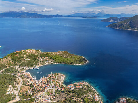 Aerial view of the turquoise waters embracing the rugged coastline, where the quaint village nestles among the verdant hills of Fiskardo, Cephalonia, Greece.