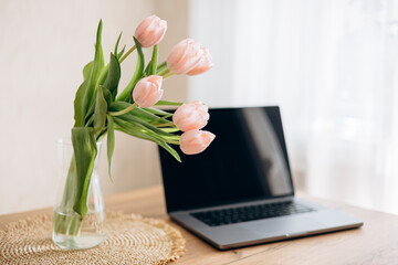 A bouquet of tulips in a vase and a laptop on a table in a cozy interior.