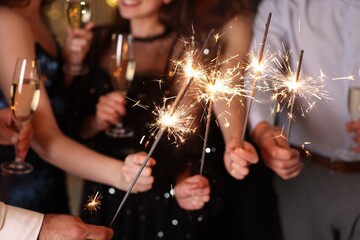 Friends celebrating New Year with sparklers and wine glasses indoors, closeup