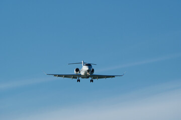 A private jet approaches the airfield against a backdrop of a partly cloudy sky. Airplane in the blue sky with white clouds.