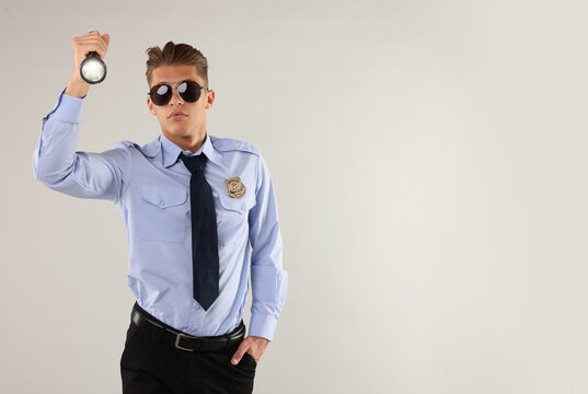 Young policeman in uniform with flashlight on light grey background, space for text