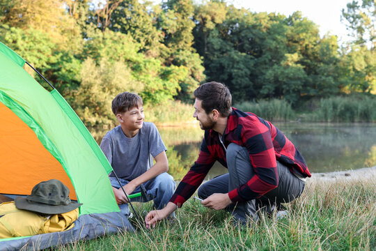 Happy father and son setting up camping tent near river outdoors