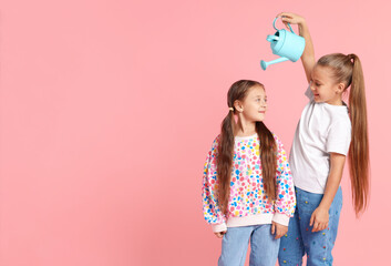 Little girl holding watering can above her friend on pink background, space for text. Grow up faster