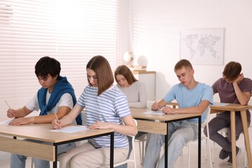 Students taking exam at wooden table indoors