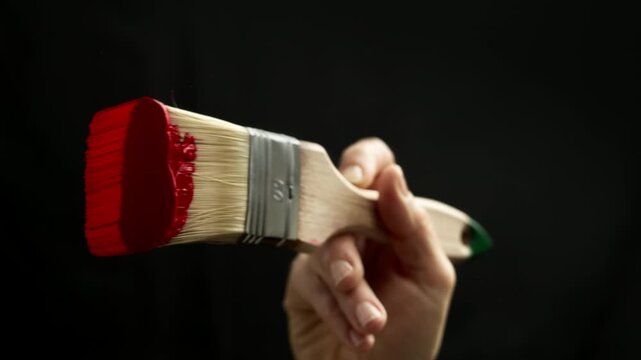Close-up of a brush with red acrylic paint applied by an artist to glass against a black background. Design concept. Texture.