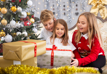 Two girls and boy holding gift in Christmas interior