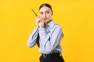 Young policewoman in uniform with walkie talkie on yellow background