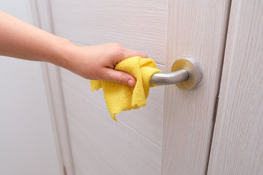 Woman hand cleaning door handle with yellow microfiber cloth. Household chore and daily hygiene concept. Disinfection surface to prevent germs.